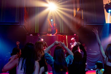 Bir grup insan disko gece kulübünde DJ 'in sahnede çaldığı müzikle dans ediyor.