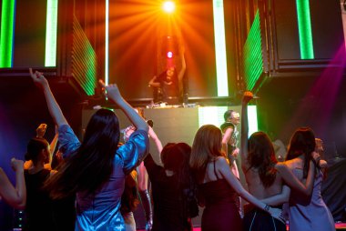 Bir grup insan disko gece kulübünde DJ 'in sahnede çaldığı müzikle dans ediyor.