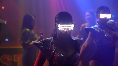 Bir grup insan disko gece kulübünde DJ 'in sahnede çaldığı müzikle dans ediyor.