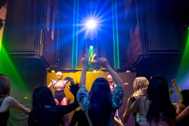 Bir grup insan disko gece kulübünde DJ 'in sahnede çaldığı müzikle dans ediyor.