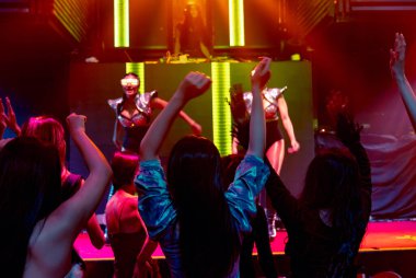 Bir grup insan disko gece kulübünde DJ 'in sahnede çaldığı müzikle dans ediyor.