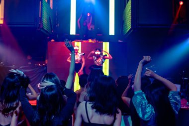 Bir grup insan disko gece kulübünde DJ 'in sahnede çaldığı müzikle dans ediyor.