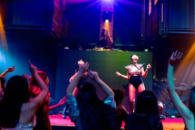 Bir grup insan disko gece kulübünde DJ 'in sahnede çaldığı müzikle dans ediyor.