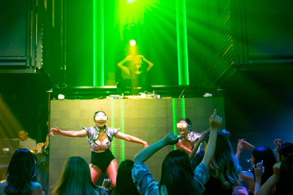 Grupp av människor dansar i disco nattklubb till rytmen av musik från DJ på scenen — Stockfoto