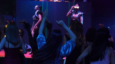Bir grup insan disko gece kulübünde DJ 'in sahnede çaldığı müzikle dans ediyor.