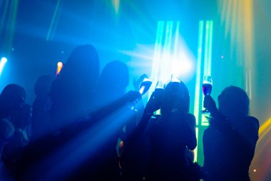 Disko gece kulübünde DJ 'in sahnede yaptığı müzikle dans eden insanların silueti.