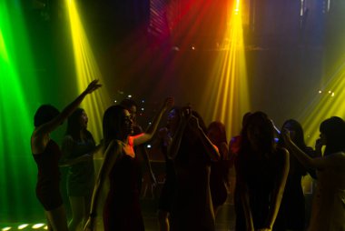 Disko gece kulübünde DJ 'in sahnede yaptığı müzikle dans eden insanların silueti.
