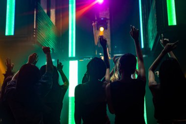 Disko gece kulübünde DJ 'in sahnede yaptığı müzikle dans eden insanların silueti.
