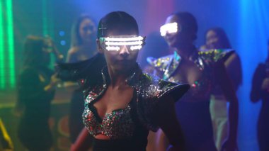 Bir grup insan disko gece kulübünde DJ 'in sahnede çaldığı müzikle dans ediyor.