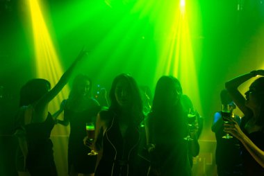 Disko gece kulübünde DJ 'in sahnede yaptığı müzikle dans eden insanların silueti.