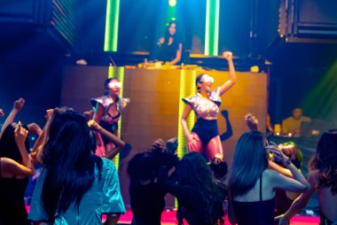 Bir grup insan disko gece kulübünde DJ 'in sahnede çaldığı müzikle dans ediyor.