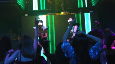 Bir grup insan disko gece kulübünde DJ 'in sahnede çaldığı müzikle dans ediyor.