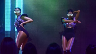 Bir grup insan disko gece kulübünde DJ 'in sahnede çaldığı müzikle dans ediyor.