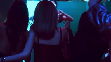 Bir grup insan disko gece kulübünde DJ 'in sahnede çaldığı müzikle dans ediyor.