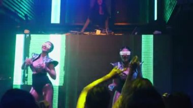 Bir grup insan disko gece kulübünde DJ 'in sahnede çaldığı müzikle dans ediyor.