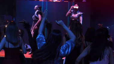 Bir grup insan disko gece kulübünde DJ 'in sahnede çaldığı müzikle dans ediyor.