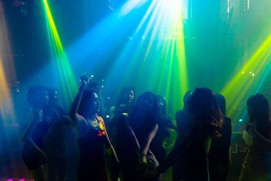 Disko gece kulübünde DJ 'in sahnede yaptığı müzikle dans eden insanların silueti.