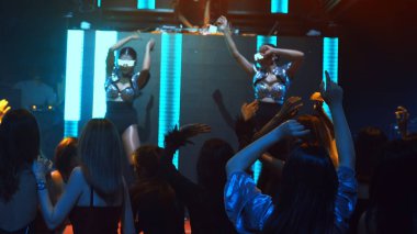 Bir grup insan disko gece kulübünde DJ 'in sahnede çaldığı müzikle dans ediyor.