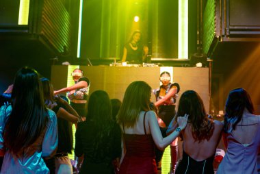 Bir grup insan disko gece kulübünde DJ 'in sahnede çaldığı müzikle dans ediyor.