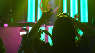 Bir grup insan disko gece kulübünde DJ 'in sahnede çaldığı müzikle dans ediyor.