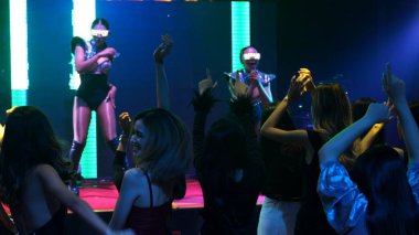 Bir grup insan disko gece kulübünde DJ 'in sahnede çaldığı müzikle dans ediyor.