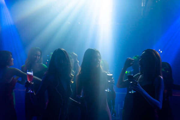 Silhouette image of people dance in disco night club to music from DJ on stage