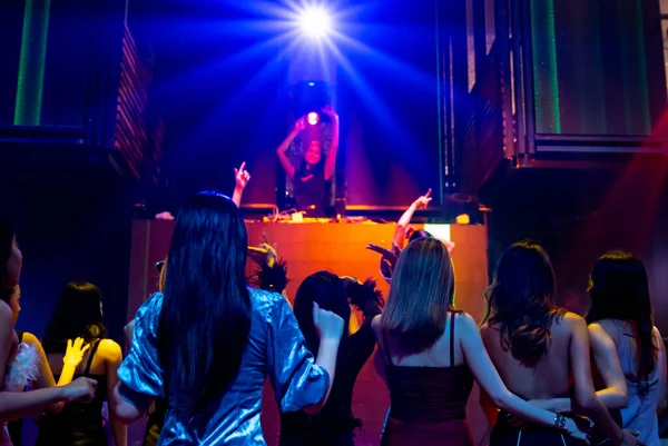 Bir grup insan disko gece kulübünde DJ 'in sahnede çaldığı müzikle dans ediyor.