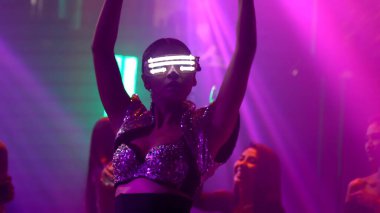 Bir grup insan disko gece kulübünde DJ 'in sahnede çaldığı müzikle dans ediyor.