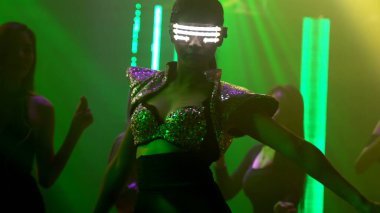 Bir grup insan disko gece kulübünde DJ 'in sahnede çaldığı müzikle dans ediyor.