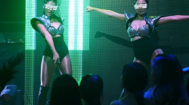 Bir grup insan disko gece kulübünde DJ 'in sahnede çaldığı müzikle dans ediyor.