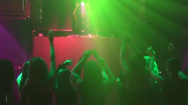 Bir grup insan disko gece kulübünde DJ 'in sahnede çaldığı müzikle dans ediyor.