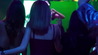 Bir grup insan disko gece kulübünde DJ 'in sahnede çaldığı müzikle dans ediyor.