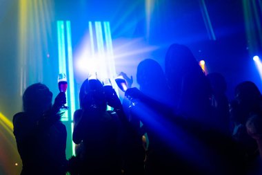 Disko gece kulübünde DJ 'in sahnede yaptığı müzikle dans eden insanların silueti.