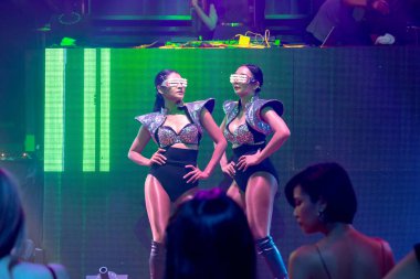 Bir grup insan disko gece kulübünde DJ 'in sahnede çaldığı müzikle dans ediyor.