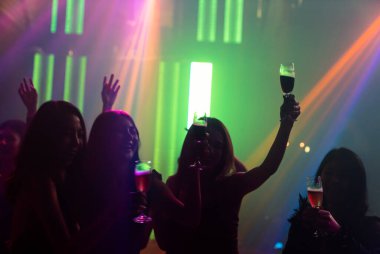Disko gece kulübünde DJ 'in sahnede yaptığı müzikle dans eden insanların silueti.