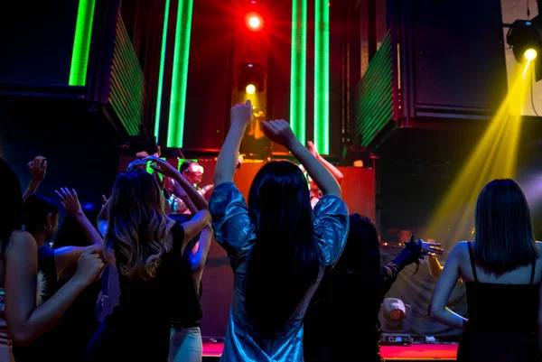 Group of people dance in disco night club to the beat of music from DJ on stage