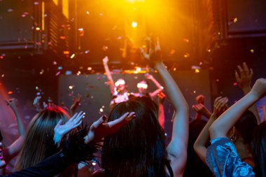 Bir grup insan disko gece kulübünde DJ 'in sahnede çaldığı müzikle dans ediyor.