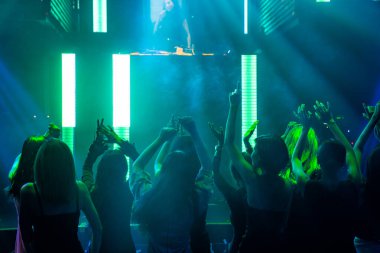Disko gece kulübünde DJ 'in sahnede yaptığı müzikle dans eden insanların silueti.