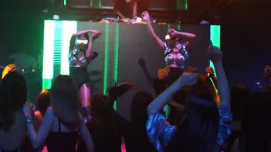 Bir grup insan disko gece kulübünde DJ 'in sahnede çaldığı müzikle dans ediyor.