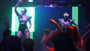 Bir grup insan disko gece kulübünde DJ 'in sahnede çaldığı müzikle dans ediyor.