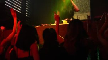 Bir grup insan disko gece kulübünde DJ 'in sahnede çaldığı müzikle dans ediyor.