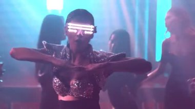 Bir grup insan disko gece kulübünde DJ 'in sahnede çaldığı müzikle dans ediyor.