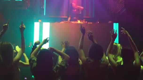 Grupo de personas bailan en discoteca al ritmo de la música de DJ en el escenario — Vídeos de Stock