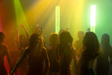 Disko gece kulübünde DJ 'in sahnede yaptığı müzikle dans eden insanların silueti.