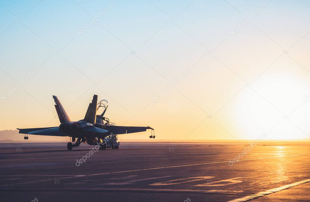 Jet fighter on an aircraft carrier deck against beautiful sunset sky .