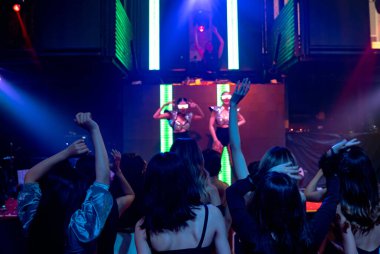 Bir grup insan disko gece kulübünde DJ 'in sahnede çaldığı müzikle dans ediyor.