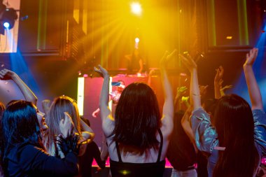Bir grup insan disko gece kulübünde DJ 'in sahnede çaldığı müzikle dans ediyor.