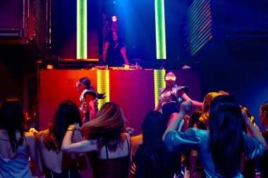 Bir grup insan disko gece kulübünde DJ 'in sahnede çaldığı müzikle dans ediyor.