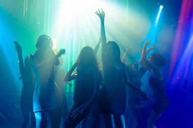 Disko gece kulübünde DJ 'in sahnede yaptığı müzikle dans eden insanların silueti.