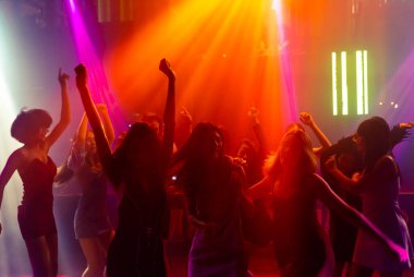Disko gece kulübünde DJ 'in sahnede yaptığı müzikle dans eden insanların silueti.